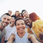 A diverse group of friends taking a joyful selfie outdoors during sunset.